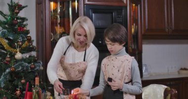 Gülümseyen kadın ve çocuk yılbaşı arifesinde evde mum yakıyor. Noel 'de evi dekore eden mutlu beyaz anne ve oğulun portresi. Sinema 4k ProRes Merkezi.