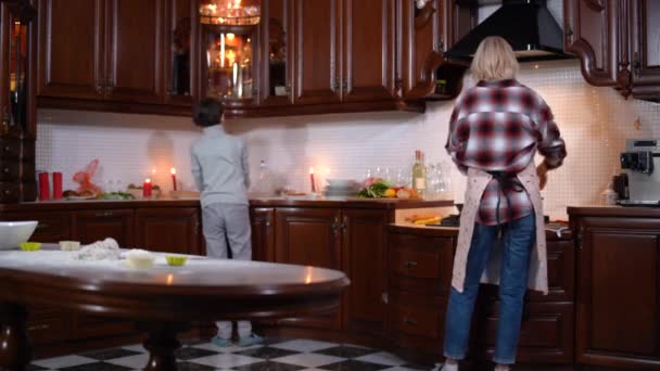 Nagy visszapillantás a fiatal anya főztjére, ahogy kisfia mosogatott. Barátságos kaukázusi család a konyhában este. Szülői és családi élet. — Stock videók