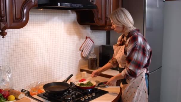 Skoncentrowana piękna kobieta smaży szparagi w kuchni w domu. Widok z boku portret blondynki pewnej siebie białej kobiety przygotowującej obiad w domu. Gotowanie i kulinarne. — Wideo stockowe