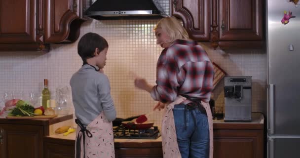 Syn piecze rękę pomagając matce w gotowaniu. Widok z tyłu na białą kobietę i chłopca przygotowujących obiad w kuchni w domu. Rodzinna kuchnia. Kino 4k ProRes kwatera główna. — Wideo stockowe