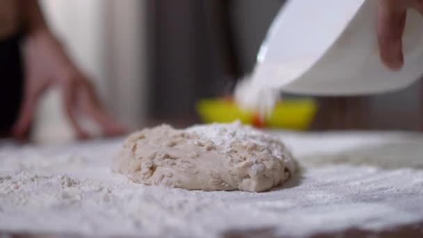 Unrecognizable woman pouring flour on pastry dough. Caucasian female adult hands and little male palms kneading raw dough on table in kitchen at home. Mother and son cooking indoors. — Stock Video