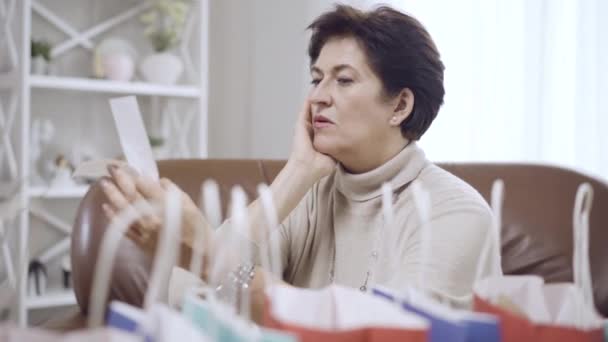 Vista lateral de la morena aturdida mujer de mediana edad mirando los billetes con la cabeza en las manos. Estresado hermosa caucásica shopper en Viernes Negro en casa. Concepto de gasto y compras. — Vídeos de Stock