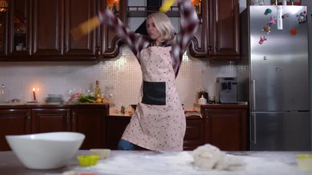 O fotografie vastă a unei tinere caucaziene care dansează în bucătărie acasă. Portret de doamnă frumoasă veselă în șorț cu gătitul distractiv în interior. Stil de viață și fericire . — Videoclip de stoc