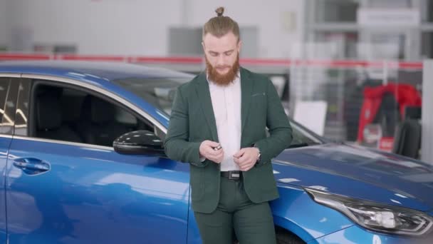 Yeni otomobilin anahtarlarıyla araba galerisinde poz veren yakışıklı sakallı beyaz adamın portresi. Zengin, kendine güveni tam bir işadamı. Galeride kameraya bakıp gülümsüyor.. — Stok video