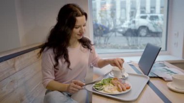 Güzel, genç, beyaz bir kadın sabahları restoranda İngiliz kahvaltısı tadıyor. Kafede yemek yiyen ve gülümseyen kendine güvenen mutlu kadının portresi. Yaşam tarzı ve eğlence..