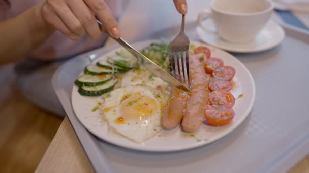 Hoge hoek uitzicht op vrouwelijke handen snijden worst op plaat in restaurant of cafe. Onherkenbare slanke blanke vrouw die ontbijt met tomaten en gebakken eieren. Dineren en lunchen concept. — Stockvideo