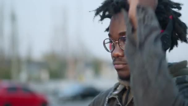 Portrait d'un jeune Afro-Américain insouciant en casque dansant et faisant des gestes à l'extérieur dans une ville urbaine au coucher du soleil. Happy gars détendu profiter de la musique dans les écouteurs sur le parking. — Video