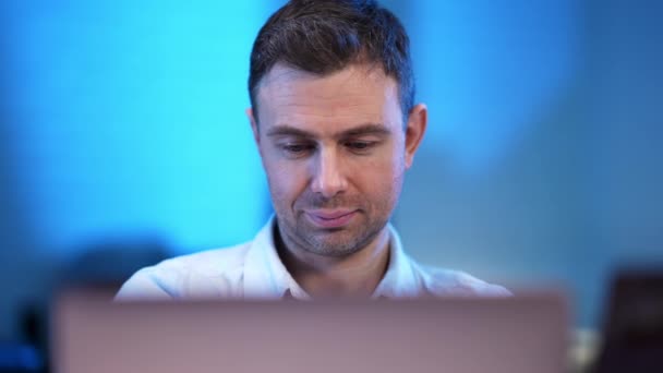 Portret przystojnego, pewnego siebie białego mężczyzny z laptopem patrzącego w kamerę. Profesjonalny haker lub programista kodowania lub hakowania strony internetowej w pomieszczeniach w niebieskim biurze. — Wideo stockowe