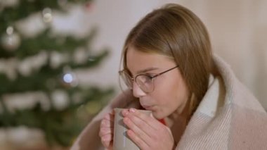 Gözlüklü esmer ergenin yeni yıl arifesinde evde çay içerken yakın çekimi. Çekici, kendine güvenen, beyaz bir kızın Noel 'de evde sıcak içkinin tadını çıkardığı yakın plan..