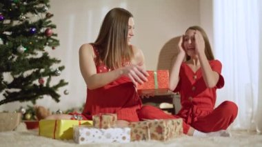 Gülümseyen hamile, beyaz bir anne yılbaşı arifesinde heyecanlı genç kızına Noel hediyesi veriyor. Evde tatilini kutlayan neşeli kadın ve kızın portresi. Eğlence ve eğlence..