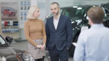 Kafası karışmış başarılı beyaz çift bayilikte yeni bir araba seçiyor. Satıcı galerideki müşterilere yaklaşıyor. Varlıklı karı koca otomobil satın alan çalışanlara danışmanlık yapıyor. Yavaş çekim.