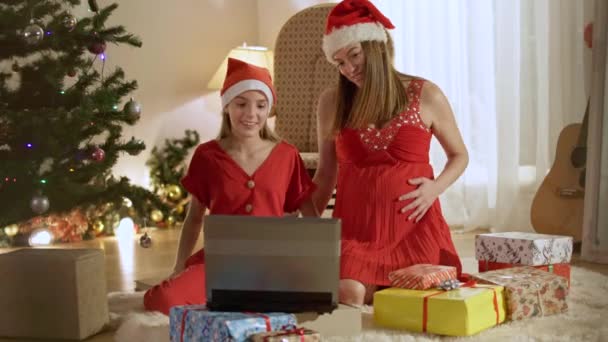 Boldog kaukázusi terhes nő és tinédzser lány karácsonyi sapkában videóbeszélgetéssel a laptopon szilveszterkor. Nyugodt mosolygó anya és lánya integetnek és beszélgetnek. Modern ünnep ünneplés. — Stock videók