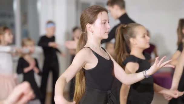 Koncentrerad vit tjej repeterar latinska balsalsdansrörelser med klasskamrater i dansskolan. Fokuserade vackra barn och tonåringar rör sig i slow motion i dansstudio. — Stockvideo