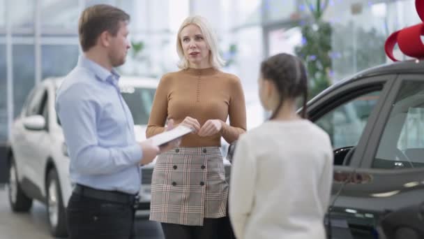 Portrét sebevědomé blondýny mluvící s prodejcem aut vybírající nové vozidlo s dcerou. Štíhlá okouzlující bělošská matka konzultuje zaměstnance v prodejně aut. Luxusní a bohatý koncept. — Stock video