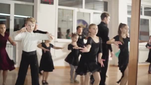 Refleksja w lustrze grupy dzieci ćwiczących latynoskie ruchy towarzyskie z chodzącym nauczycielem. utalentowani kaukascy chłopcy i dziewczęta ćwiczący sztukę w szkole tańca. — Wideo stockowe