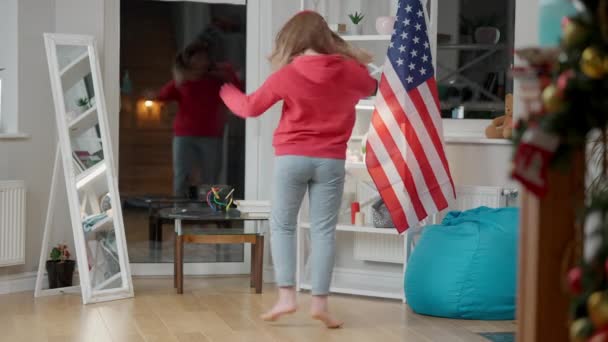 Ampla foto de adolescente alegre em fones de ouvido dançando em casa com a bandeira dos EUA no fundo. Retrato de adolescente asiático despreocupado feliz se divertindo dentro de casa desfrutando playlist. Alegria e estilo de vida. — Vídeo de Stock