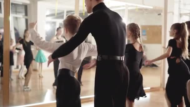 Вчитель танцю виправляє позу маленького хлопчика, який репетирує в танцювальній студії. Молодий кавказький чоловік навчає дітей танцювати. Талант і мистецтво. — стокове відео