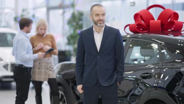 Glad skäggig gråhårig man tittar på bilnyckeln och gester glädje inköp av lyxiga fordon i bilhandlare. Porträtt av framgångsrik vit klient poserar i showroom. — Stockvideo