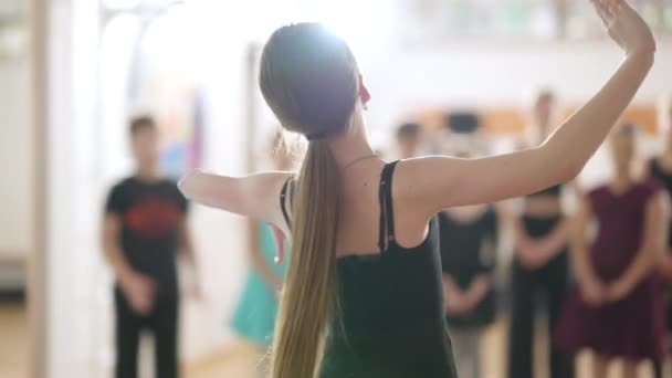 Câmera segue magro menina caucasiana waltzing na quarta posição com grupo de crianças desfocadas assistindo. Criança talentosa mostrando movimento de balé para colegas na escola de dança. Habilidade e arte. — Vídeo de Stock