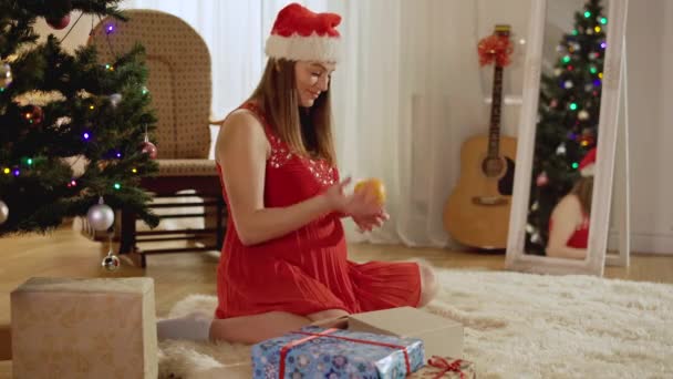 Позитивна вагітна жінка бігає і пахне помаранчевим сидячи вдома в новорічну ніч. Портрет щасливого кавказького довгоочікуваного святкування Різдва в приміщенні. Радість і дозвілля. — стокове відео