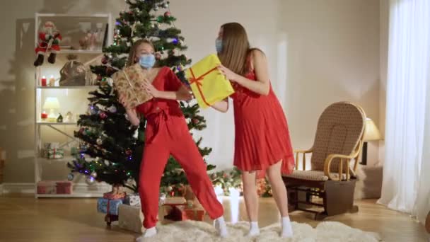 Foto wanita hamil ceria dan gadis remaja bertopeng wajah coronavirus menari dengan hadiah Natal di rumah. Portrait of joyful Caucasian mother and daughter having fun on New Year. — Stok Video