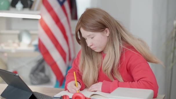 集中天才アジアの10代の少女がアメリカ国旗を背景にテーブルに座って宿題をしています。アメリカで学ぶスマート10代の留学生の肖像画。教育理念. — ストック動画