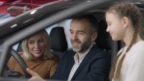 차에 앉아서 여성과 소녀와 이야기하는 긍정적 인 수염을 가진 사업가. 가족의 대리점에서 새 차를 사는 자신있는 행복 한 남편과 아버지의 모습. 선택과 성공 개념. — 비디오