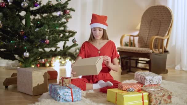 Portret cu o adolescentă entuziasmată care deschide cadoul de Crăciun și zâmbește. Un adolescent caucazian fericit, fără griji, care primește cadou în ajunul Anului Nou acasă în interior. Fericire și surpriză . — Videoclip de stoc