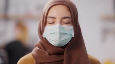 Covid-19 yüz maskesi takmış genç ve güzel bir Orta Doğulu kadının kamera karşısında fotoğrafı. Üzücü bin yılın yakın plan portresi. Kahverengi gözlü. Koronavirüs salgınında içeride poz veriyor..