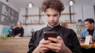 Orta Doğulu genç bir adam kıvırcık saçlı ve kahverengi gözlü sosyal medyayı akıllı telefondan kullanıyor. Cafe 'de dinlenip düzeni bekleyen yakışıklı milenyumun portresi..