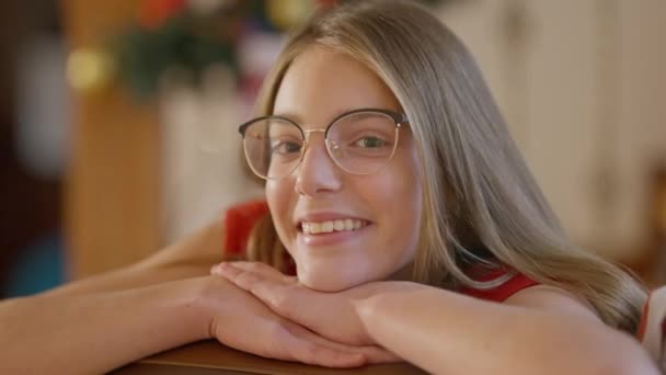 Potret gadis remaja Kaukasia yang gembira dengan kacamata menatap kamera sambil tersenyum. Headshot dari remaja gembira santai berpose di rumah dalam ruangan pada malam Natal. Konsep kebahagiaan. — Stok Video