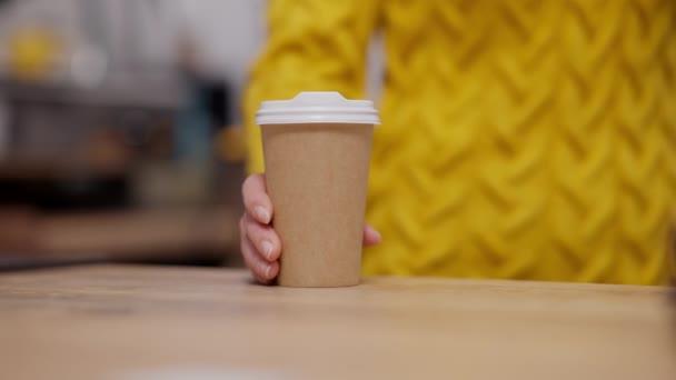 Joven mujer caucásica mano empujando taza de café desechable a la cámara. Barista irreconocible que sirve bebidas calientes en la cafetería o cafetería. Ocupación de servicios. — Vídeo de stock