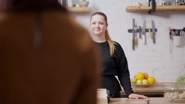 Retrato de camarera profesional positiva saludando al cliente en cafetería. Mujer caucásica sonriente hablando con una clienta de Oriente Medio en Hiyab. Negocio y diversidad de restaurantes. — Vídeo de stock