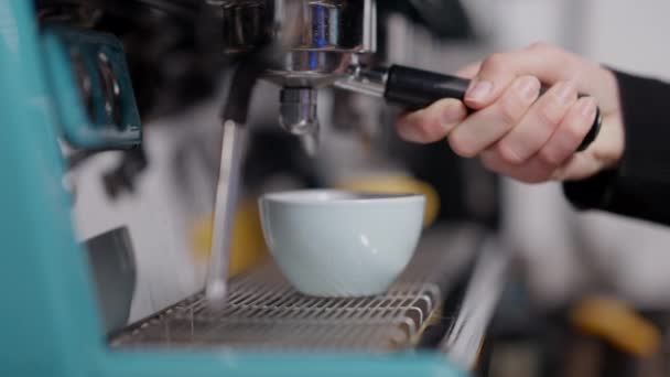 Side view close-up van vrouwelijke hand bevestigd portafilter aan koffiemachine in slow motion. Warme espresso die stroomt in een blauwe beker in de kantine. Bereiding van lekkere verse drank in café of restaurant. — Stockvideo