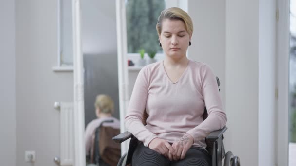 Porträt einer jungen gestressten querschnittsgelähmten Frau, die im Rollstuhl sitzt, in die Kamera schaut und betet. Nahaufnahme eines deprimierten traurigen kaukasischen Invaliden, der auf das Beste hofft. Zeitlupe. — Stockvideo