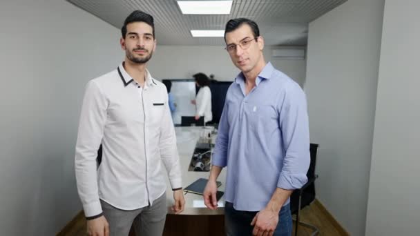 Ritratto di fiduciosi uomini mediorientali di successo che posano in ufficio incrociando le mani e guardando la fotocamera. Millennial dipendenti in piedi sul posto di lavoro con le donne discutendo start-up in background. — Video Stock