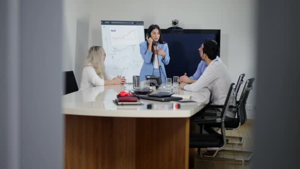 Retrato de tiro largo de mulher asiática bonita falando no telefone de escritório e contando boas notícias a colegas. Colegas alegres se alegrando com o sucesso na sala de conferências. A disparar pela porta.. — Vídeo de Stock