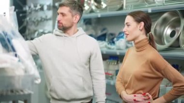 Hırdavatçıda güzel bir kadınla konuşan yakışıklı bir adamın portresi. Minnettar bir eş kocaya sarılmış gibi. Heyecanlı Kafkas kız arkadaşı tavsiyesi için erkek arkadaşına teşekkür ediyor..