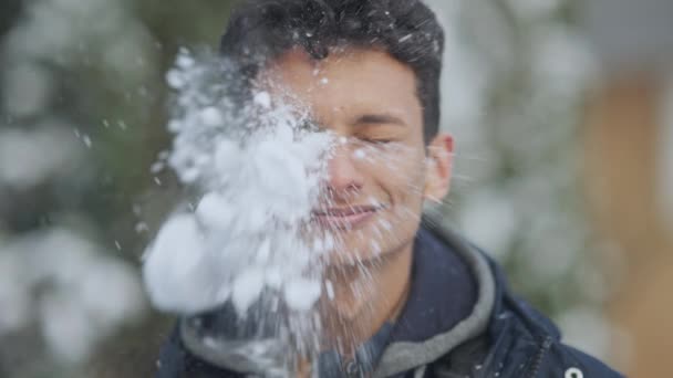 Boule de neige frappant le visage du jeune homme souriant du Moyen-Orient au ralenti. Gros plan portrait d'un gars surpris par une journée enneigée en plein air. Bataille de boule de neige et concept d'hiver. — Video