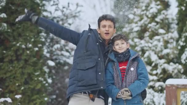 Bliski rzut pozytywnego nastolatka i młodsi bracia rzucający śniegiem w zwolnionym tempie patrząc w kamerę. Portret wesołych, beztroskich chłopców z Bliskiego Wschodu cieszących się śnieżną pogodą na świeżym powietrzu. Styl życia i radość. — Wideo stockowe