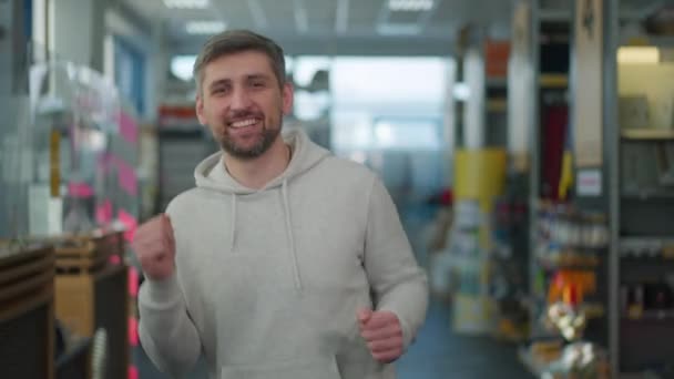 Vrolijke gelukkige blanke man dansend in een ijzerwinkel kijkend naar de camera. Portret van een vreugdevolle koper die plezier heeft in het bouwen van benodigdheden winkel binnen. Levensstijl en vreugde concept. — Stockvideo
