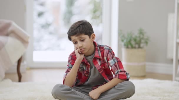 Triste garçon du Moyen-Orient frustré assis sur le tapis à la maison pensant. Portrait d'un enfant seul et déprimé, intimidé et seul à l'intérieur. Problèmes d'enfance et concept de dépression. — Video