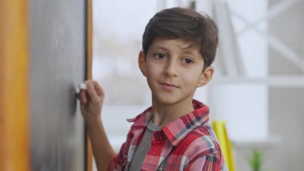 Retrato de close-up de bonito estudante do Oriente Médio escrevendo no quadro, olhando para a câmera e sorrindo. Rapaz encantador positivo posando em sala de aula na escola dentro de casa. — Vídeo de Stock
