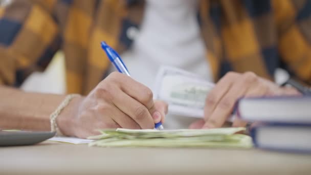 Zbliżenie męskich rąk piszących na papierze i liczących gotówkę. Nierozpoznawalny młody człowiek z Bliskiego Wschodu, obliczający dochód w domu, siedzący przy stole. Koncepcja bogactwa i finansów. — Wideo stockowe