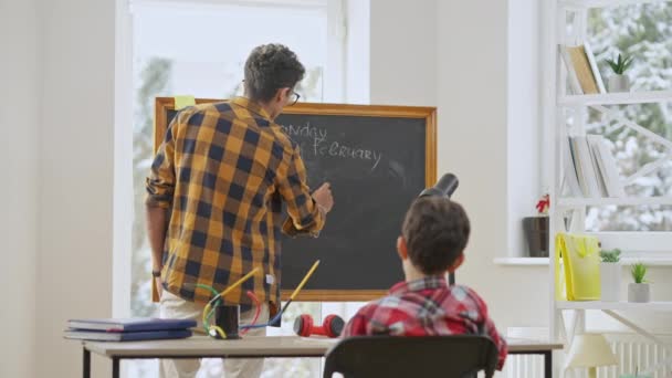 Skoncentrowany młody nauczyciel z Bliskiego Wschodu w okularach piszący na tablicy i mówiący w zwolnionym tempie jako znudzony uczeń źle się zachowujący z przodu. Nauczyciel w klasie szkolnej. — Wideo stockowe