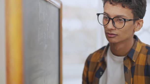 Portrét koncentrovaného studenta v brýlích, jak píše na tabuli ve třídě. Zaměřený přemýšlivý chytrý teenager studující na vysoké škole nebo na univerzitě. Vzdělávání a inteligence. — Stock video