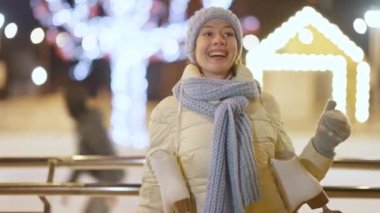 Şehir gecesinde buz patenleriyle dans eden neşeli, gülümseyen genç bir kadının portresi. Mutlu Kafkasya milenyumu Noel buz pateni sahasında poz veriyor. Boş zaman konsepti.