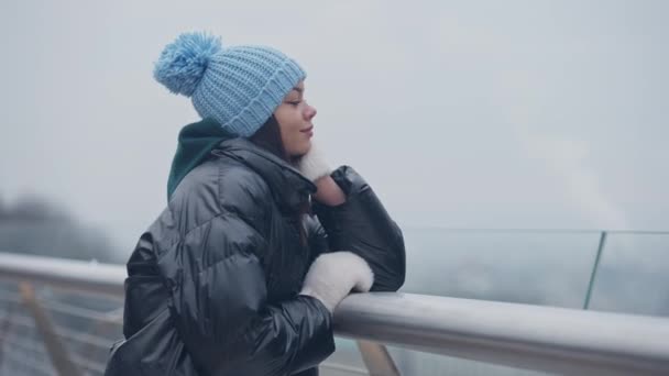 Zrelaksowana czarująca Afroamerykanka stojąca na mostku w mglisty zimowy dzień marzeń. Piękny uśmiech młodych tysiącleci korzystających z wypoczynku na świeżym powietrzu. Koncepcja kobiecości i stylu życia. — Wideo stockowe