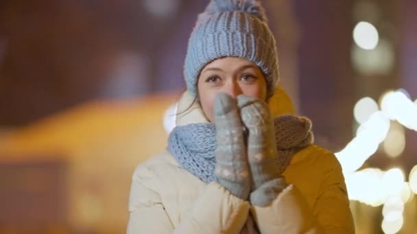 在圣诞前夕，穿着冬帽和手套站在夜市的快乐美丽的、瘦弱的高加索女人的中间镜头。在冬日的户外休闲活动中，笑着放松的千禧形象. — 图库视频影像
