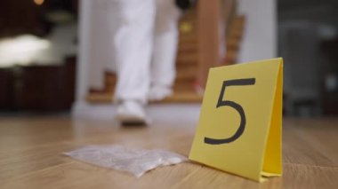 Üzerinde numaralandırılmış haplar olan şeffaf bir paket. Arka planda beyaz üniformalı bulanık dedektif merdivenlerden çıkıyor. Suç mahallinde intihar delili. Adli bilim konsepti.